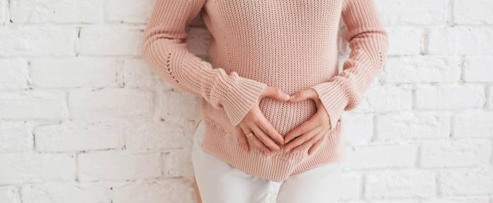 Junge Frau hält sich die Hände in Form eines Herzens vor den Bauch